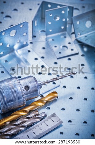 Metal ruler power drill bits and angle bars on perforated metallic background construction concept.