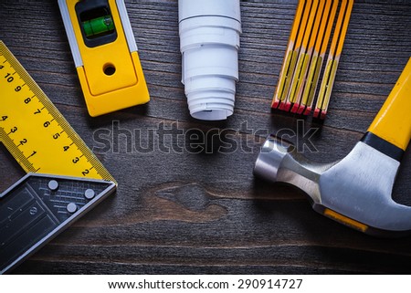 Yellow construction level try square rolled up white blueprint wooden meter and hammer on vintage wood surface maintenance concept.