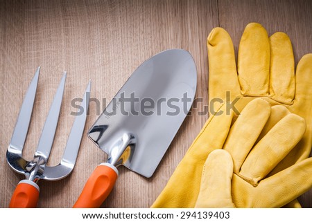 Metal hand spade trowel fork and leather safety gloves on wooden board gardening concept.