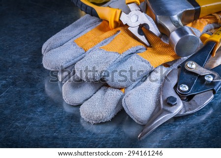 Protective gloves with claw hammer pliers and tin snips on scratched vintage metallic background construction concept.