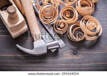 Close up image of planer claw hammer metal chisels and wooden curled shavings on vintage wood board construction concept.