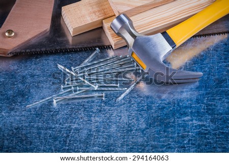 Close-up image of metal nails hammer wooden bricks hacksaw on scratched metallic surface construction concept.