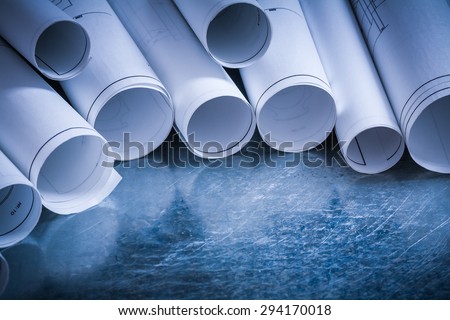 Set of rolled up white construction drawings on scratched silver-metal surface building and architecture concept.