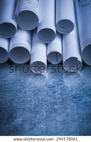 Pile of rolled engineering drawings on scratched silver-metal background building and architecture concept.