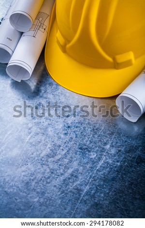 Rolled up construction plans and safety hard hat on metallic background building and architecture concept.