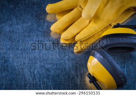 Noise reduction yellow headphones and leather protective gloves on scratched metallic background construction concept.