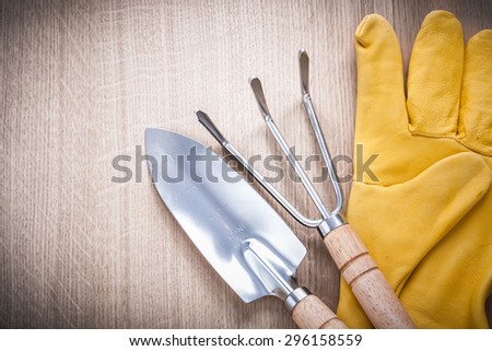 Stainless gardening trowel fork with hand spade and leather safety gloves on wooden board agriculture concept.