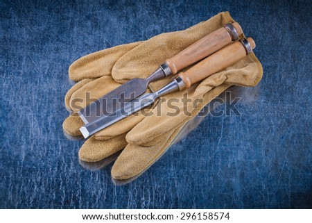 Flat chisels and pair of leather protective gloves on scratched metallic background construction concept.