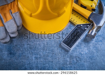 Square ruler safety gloves tape-measure building helmet and claw hammer on scratched metallic surface construction concept.