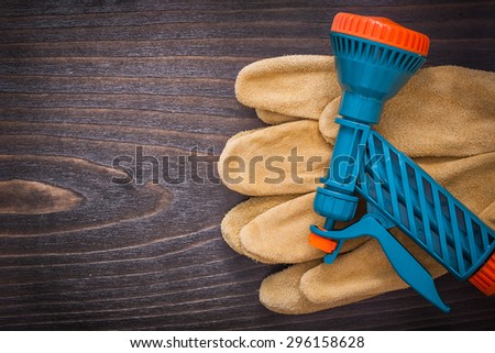 Spray nozzle and leather working safety gloves on wooden board gardening concept.