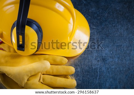 Hard hat ear muffs and leather protective gloves on metallic background close up view construction concept.