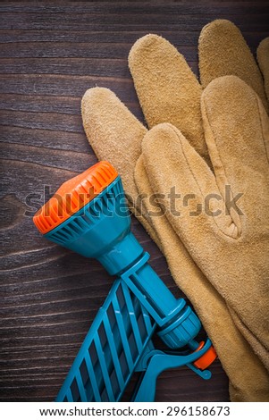 Spray water hose nozzle and leather protective gloves on wooden board gardening concept.