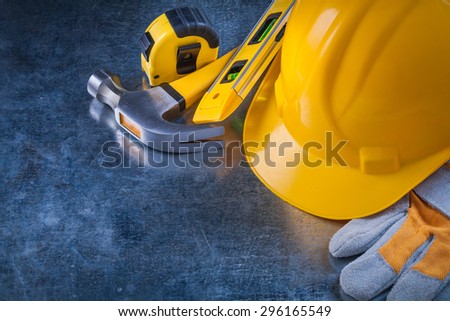 Protective gloves building helmet construction level tape-line and metal claw hammer on scratched metallic background maintenance concept.