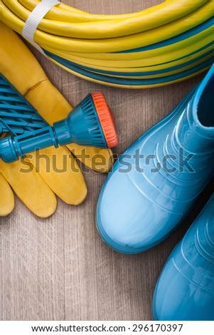 Hand spraying rubber hose with spray nozzle leather safety gloves and gumboots on wood board gardening concept.