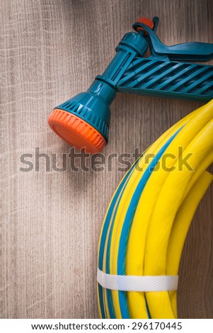 Hand spraying rubber garden hose with spray nozzle on wooden board gardening concept.