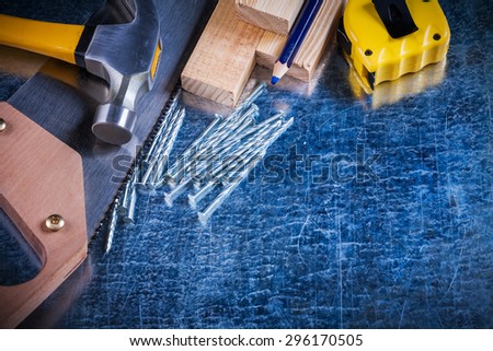 Construction nails hammer wooden bricks hand saw pencil and tape-line on scratched metallic surface maintenance concept.