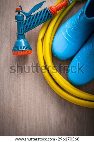 Coiled hand spraying rubber hose with spray nozzle and gum boots on wooden board gardening concept.
