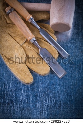 Wooden mallet firmer chisels and safety gloves on scratched metallic surface construction concept.