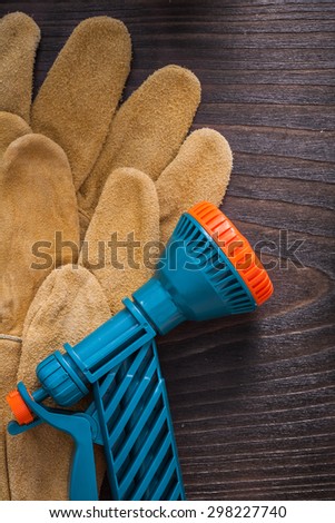 Plastic water sprayer and leather working safety gloves on wooden board gardening concept.