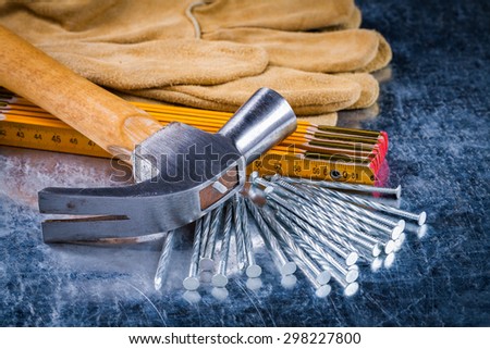 Set of leather construction gloves nails wooden measuring meter and claw hammer on scratched metallic background building concept.