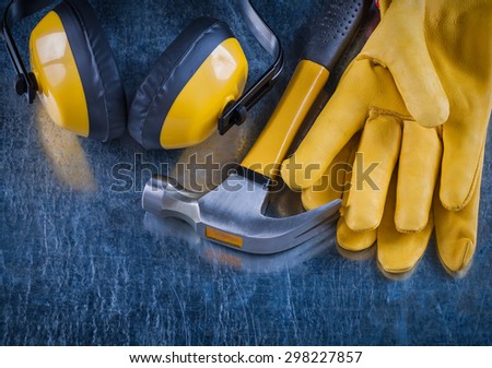 Safety yellow earmuffs claw hammer and leather construction gloves on scratched metallic surface building concept.