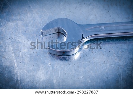 Stainless spanner wrench on scratched metallic background top view construction concept.