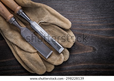 Pair of brown leather gloves with firmer chisels on vintage wooden board top view image construction concept.