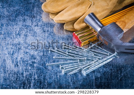Leather construction gloves nails wooden meter and claw hammer on scratched metallic surface building concept.