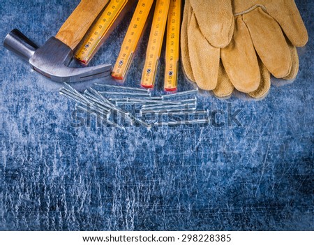 Group of protective working gloves nails wooden measuring meter and claw hammer on scratched metallic background construction concept.