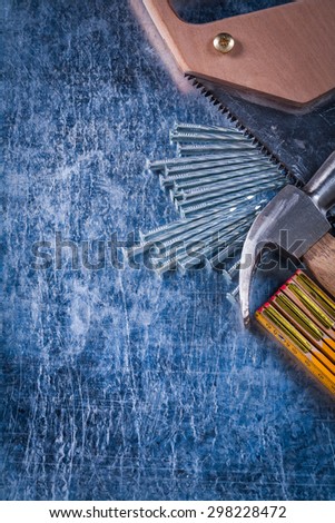 Hand saw construction nails wooden meter and claw hammer on scratched metallic background building concept.