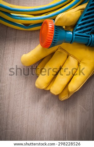 Gardening working protective gloves and hand spraying hose with spray nozzle on wooden surface agriculture concept.