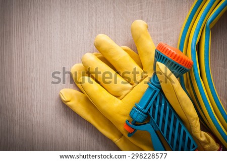 Leather gardening working safety glove and hand spraying hose with spray nozzle on wooden board agriculture concept.