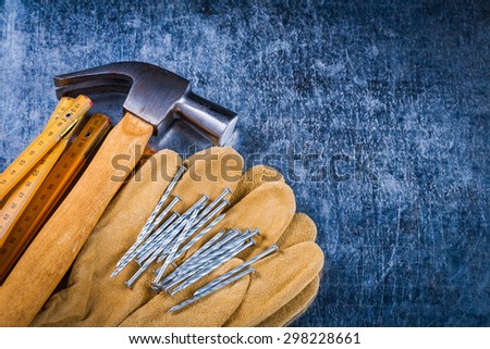 Leather protective working gloves construction nails wooden meter and claw hammer on scratched metallic surface building concept.