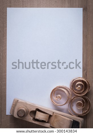 Wooden shaving plane curled planning chips and clean sheet of paper on wood board copy space image construction concept.