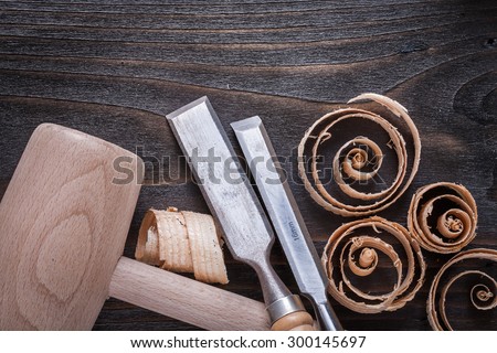 Wooden mallet chisels and curled up planing chips on vintage wood board construction concept.