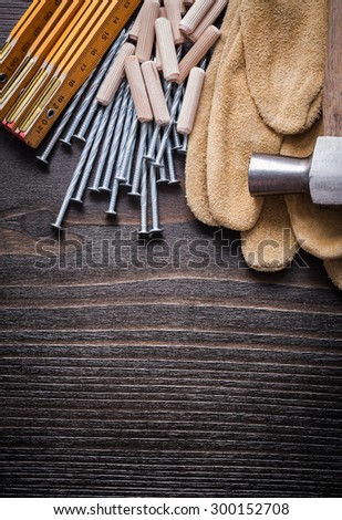 Wooden meter heap of dowels claw hammer brown protective gloves and metal nails on vintage wood board top view construction concept.