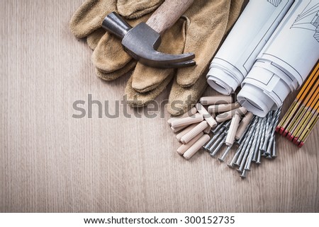 Wooden meter dowels blueprint rolls claw hammer leather protective gloves and metal nails on wood board construction concept.