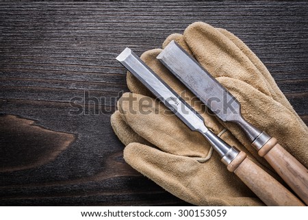 Pair of leather working gloves with flat chisels on vintage wooden board construction concept.