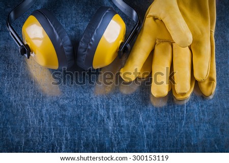 Noise reduction earmuffs and leather safety gloves on scratched metallic surface construction concept.