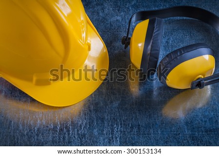 Safety yellow ear muffs and work helmet on scratched metallic background close up view construction concept.