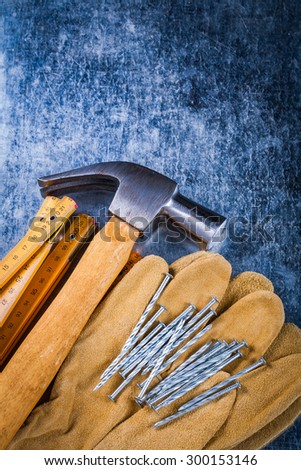 Leather safety working gloves set of construction nails wooden meter and claw hammer on scratched metallic surface building concept.