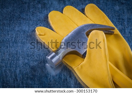 Pair of yellow construction gloves with claw hammer on scratched metallic background building concept.