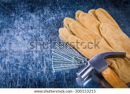 Pair of leather protective gloves construction nails and claw hammer on scratched metallic background copy space image building concept.
