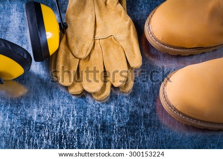 Safety boots leather gloves and noise reduction headphones on scratched metallic surface horizontal image construction concept.