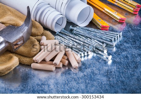 Construction drawings hammer safety gloves wooden meter metal nails and dowels on scratched metallic surface maintenance concept.