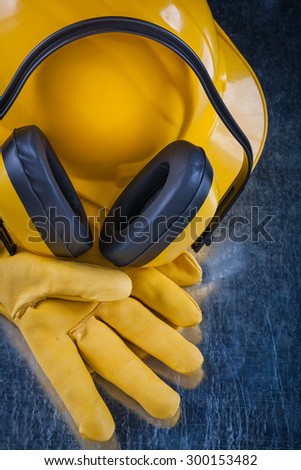 Hard hat noise reduction headphones and leather protective gloves on scratched metallic surface construction concept.