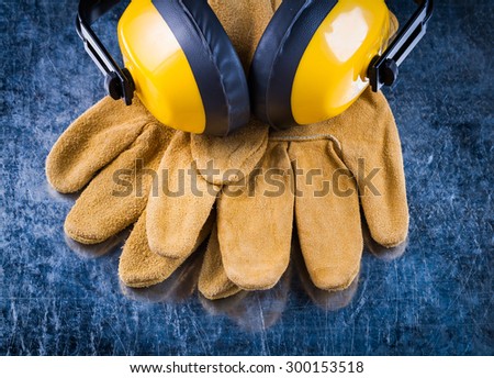 Leather safety gloves and noise insulation ear muffs on scratched metallic background construction concept.