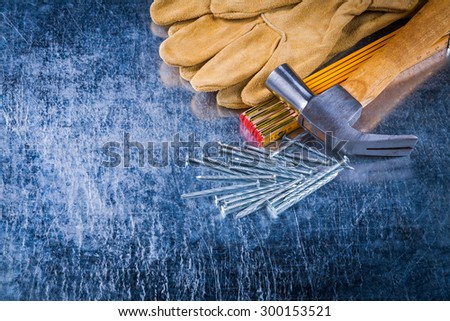 Leather construction gloves nails wooden measuring meter and claw hammer on scratched metallic background building concept.
