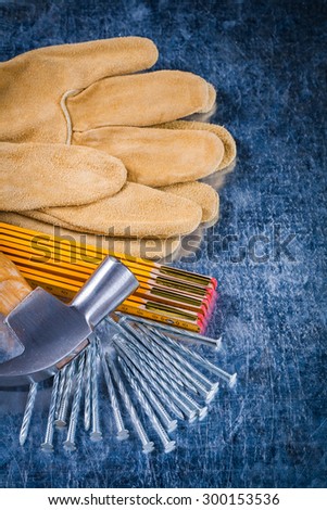 Composition of leather construction gloves nails wooden measuring meter and claw hammer on scratched metallic background building concept.