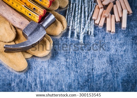 Hammer leather protective gloves wooden meter stack of metal nails and dowels on scratched metallic background construction concept.